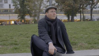 Person mit Mütze und dunkler Kleidung sitzt in einem Park