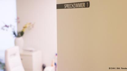 Tür mit Aufschrift "Sprechzimmer" steht offen und gewährt Blick in das Behandlungszimmer einer Praxis
