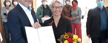 Auf dem Bild sieht man den Karlsruher OB und Karin, die beide lächelnd in die Kamera schauen. Karin trägt das Bundesverdienstkreuz und hält einen Blumenstrauß in der Hand.