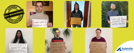 Auf dem Bild stehen sechs Personen, die Plakate in der Hand halten auf denen antirassistische Botschaften stehen. 