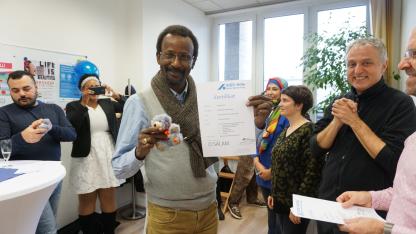 Ein Bild der Abschlussveranstaltung. Ein Mann hält sein Zertifikat in die Kamera und lächelt.