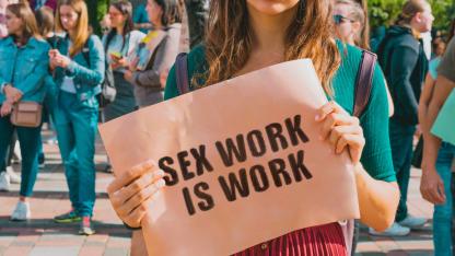 Eine Frau hält ein Schild hoch auf dem "Sex work is work" steht.